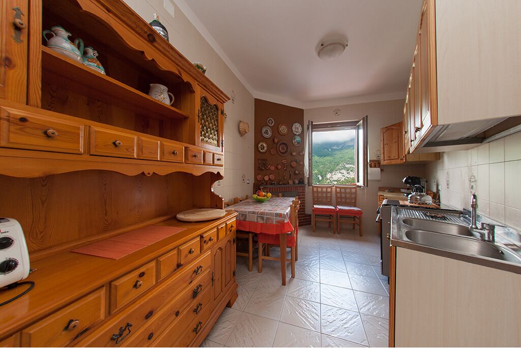 Cozinha com armários de madeira, mesa de jantar com cadeiras e vista para o exterior.