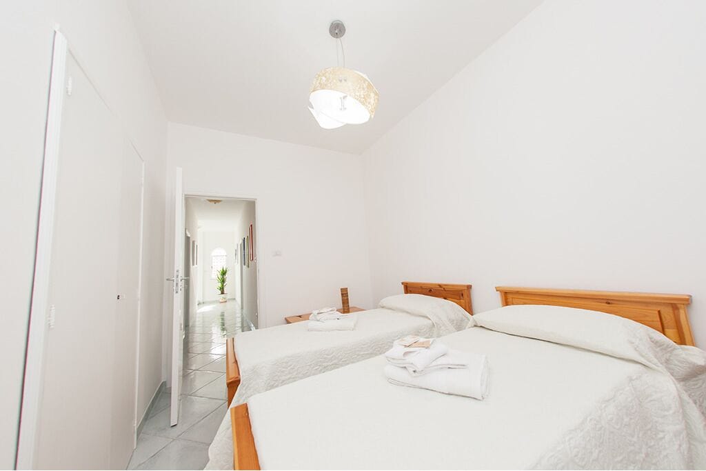 A hotel room with two beds, a wooden headboard, a white wall, and a hanging light fixture.