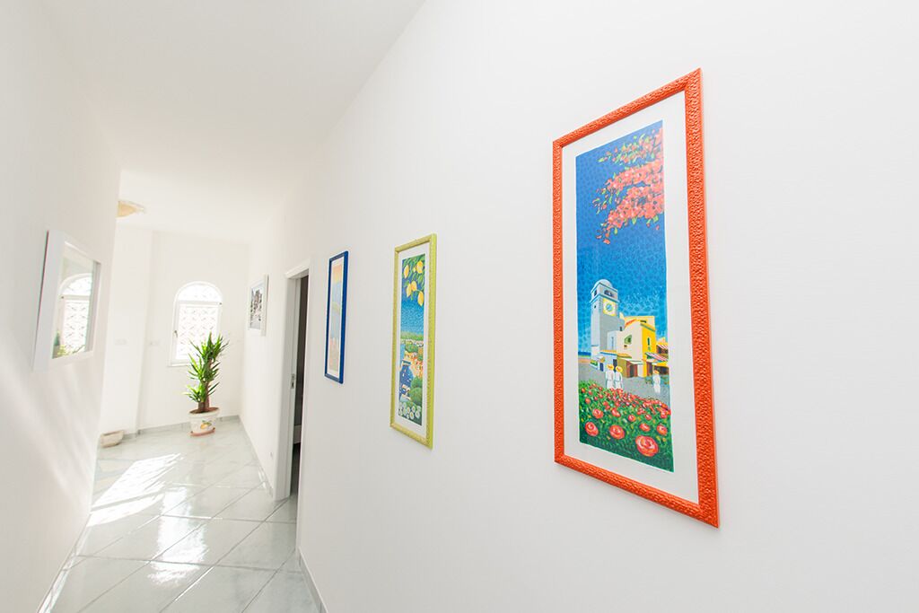 A hallway with white walls and tiled floors, featuring several framed artworks.