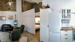 Una sala de estar con sofá, sillas, televisor y una zona de cocina con refrigerador y horno.