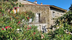 Un edificio de piedra con un balcón, rodeado de exuberante vegetación y plantas en flor.