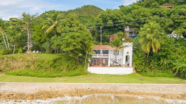 A coastal property with a white building, a staircase leading to a balcony, and lush greenery. - Casa Sack Ocean Front apartment  (Rincon)