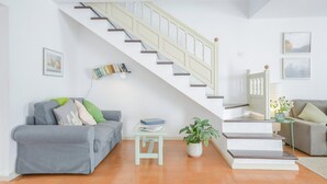 Un salon avec un escalier, des canapés gris, une petite table et une plante en pot.