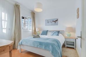 Une chambre à coucher comprenant un lit, des tables de chevet, une fenêtre avec des rideaux, un tableau accroché au mur et une lampe.