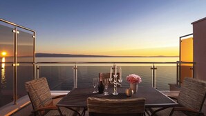 A balcony with a table set for two, overlooking a calm body of water during sunset. - Tanita Beachfront Penthouse (Podstrana)