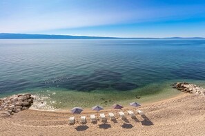 A beach with clear water, a rocky shoreline, and several sun loungers with umbrellas.