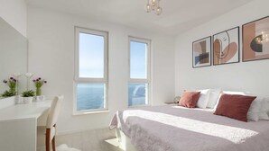 A modern bedroom with a large bed, two windows with ocean views, a desk, and a chair. - Tanita Beachfront Penthouse (Podstrana)