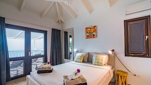 Een hotelkamer met een bed, nachtkastje, lamp, raam met gordijnen, plafondventilator en airconditioning.