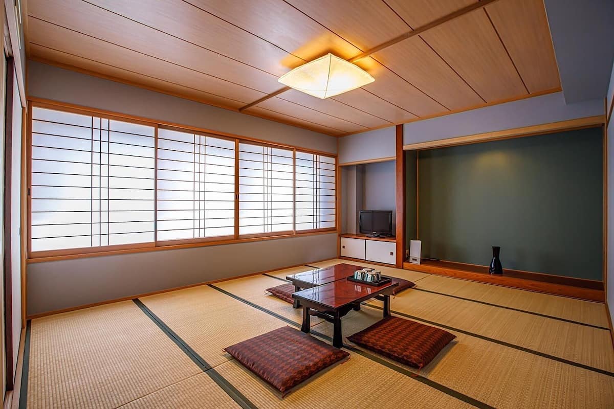 A traditional Japanese room with tatami flooring, a low table with cushions, a television, and sliding doors.
