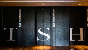 A hotel entrance with a large, dark-text elevator door featuring a prominent 'S' symbol. - The Steel House (Kitakyushu)