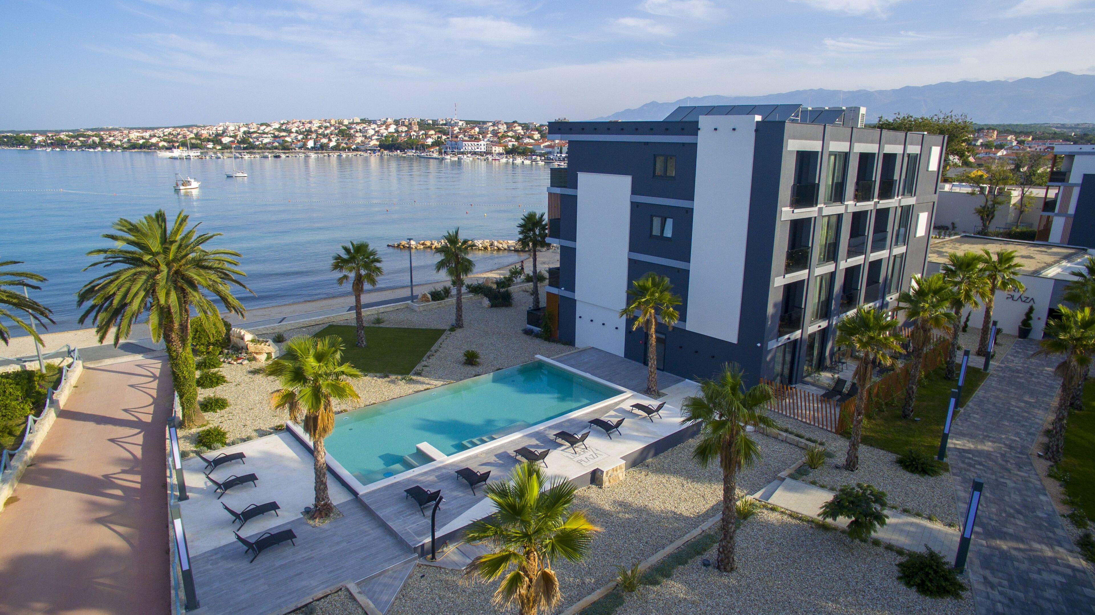 A modern hotel with a pool, palm trees, and a view of the sea.
