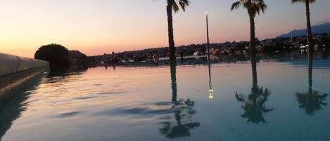 A calm infinity pool with palm trees and a sunset in the background.