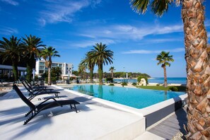 A poolside area with lounge chairs, palm trees, and a view of the sea. - Liberty Plaza (Novalja)