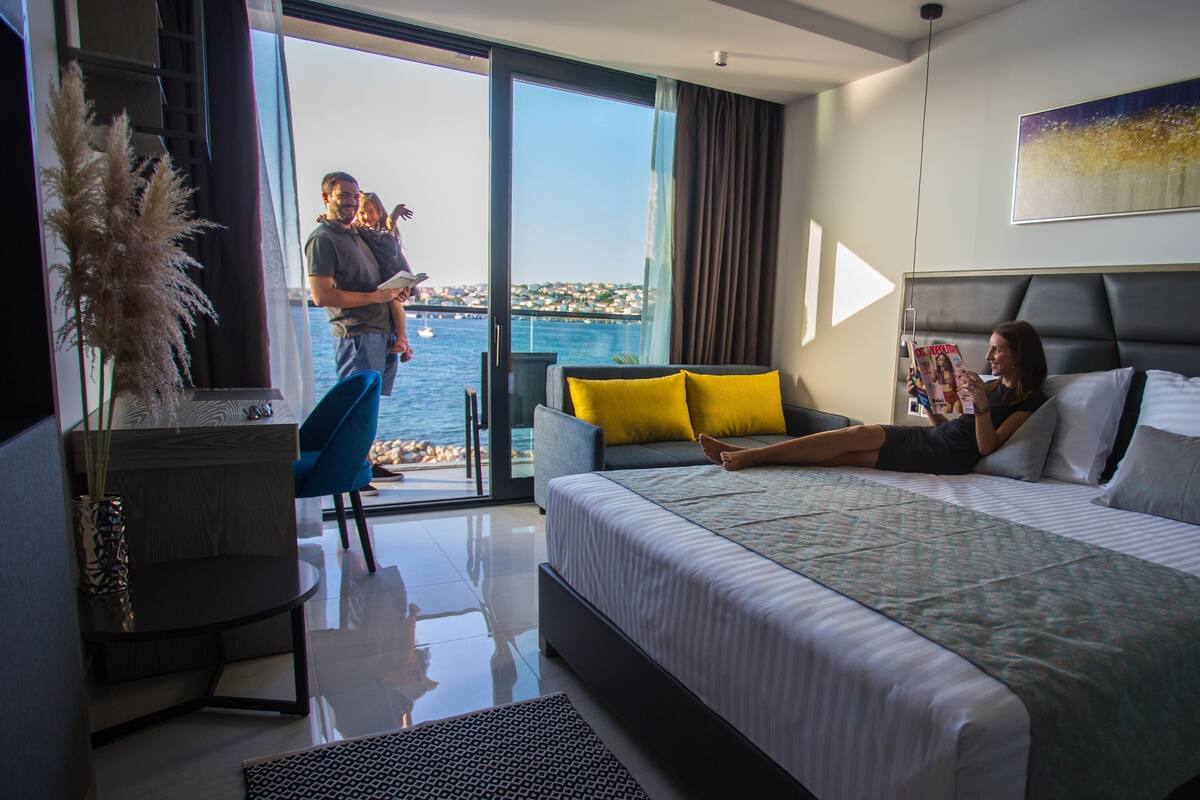 Ein modernes Hotelzimmer mit einem großen Bett, einer Couch, einem Esstisch und Meerblick.