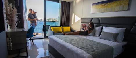 A hotel room with a bed, a sofa, a view of the sea, and a painting on the wall.