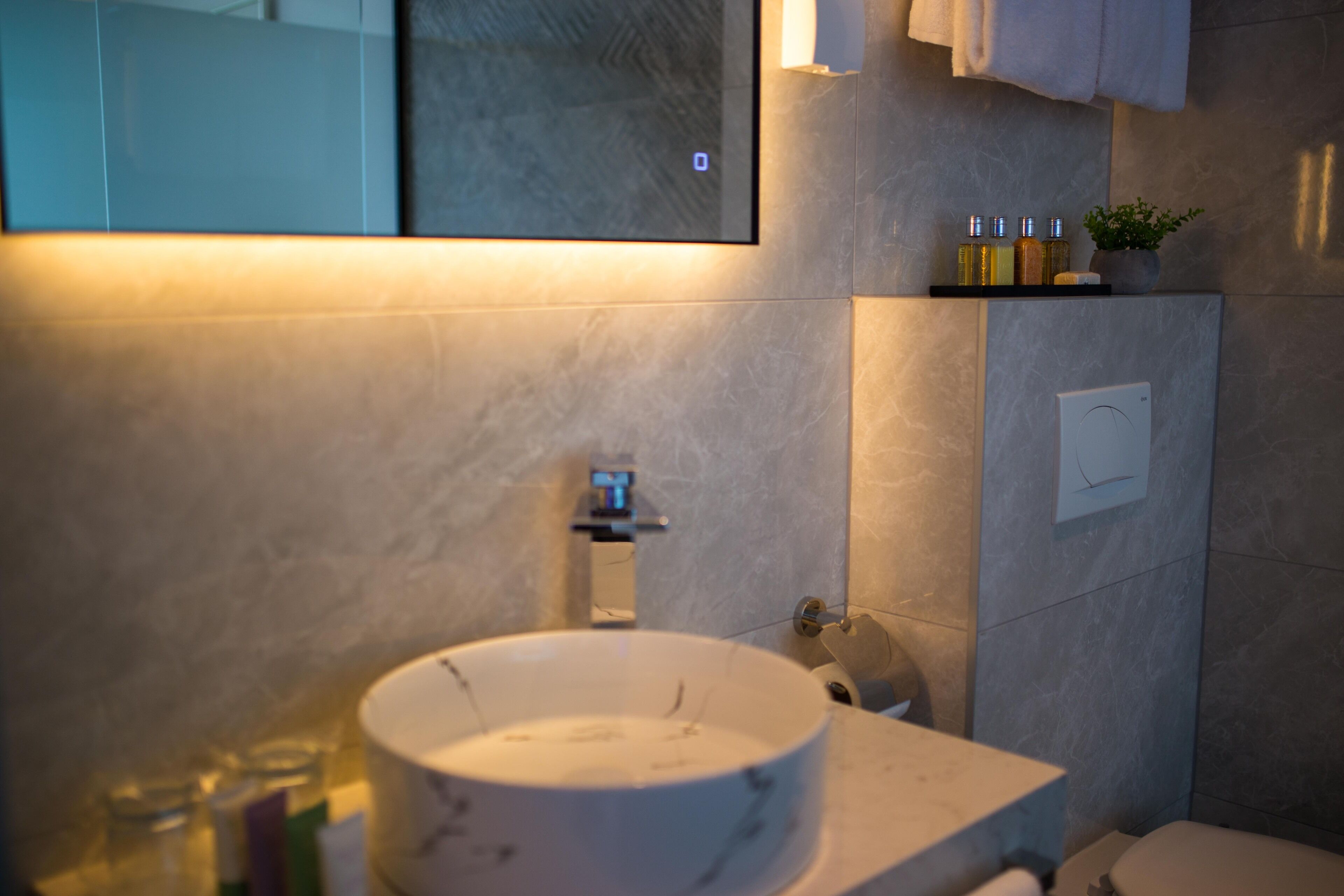 A modern bathroom with a marble sink, a mirror, and a shelf with toiletries.