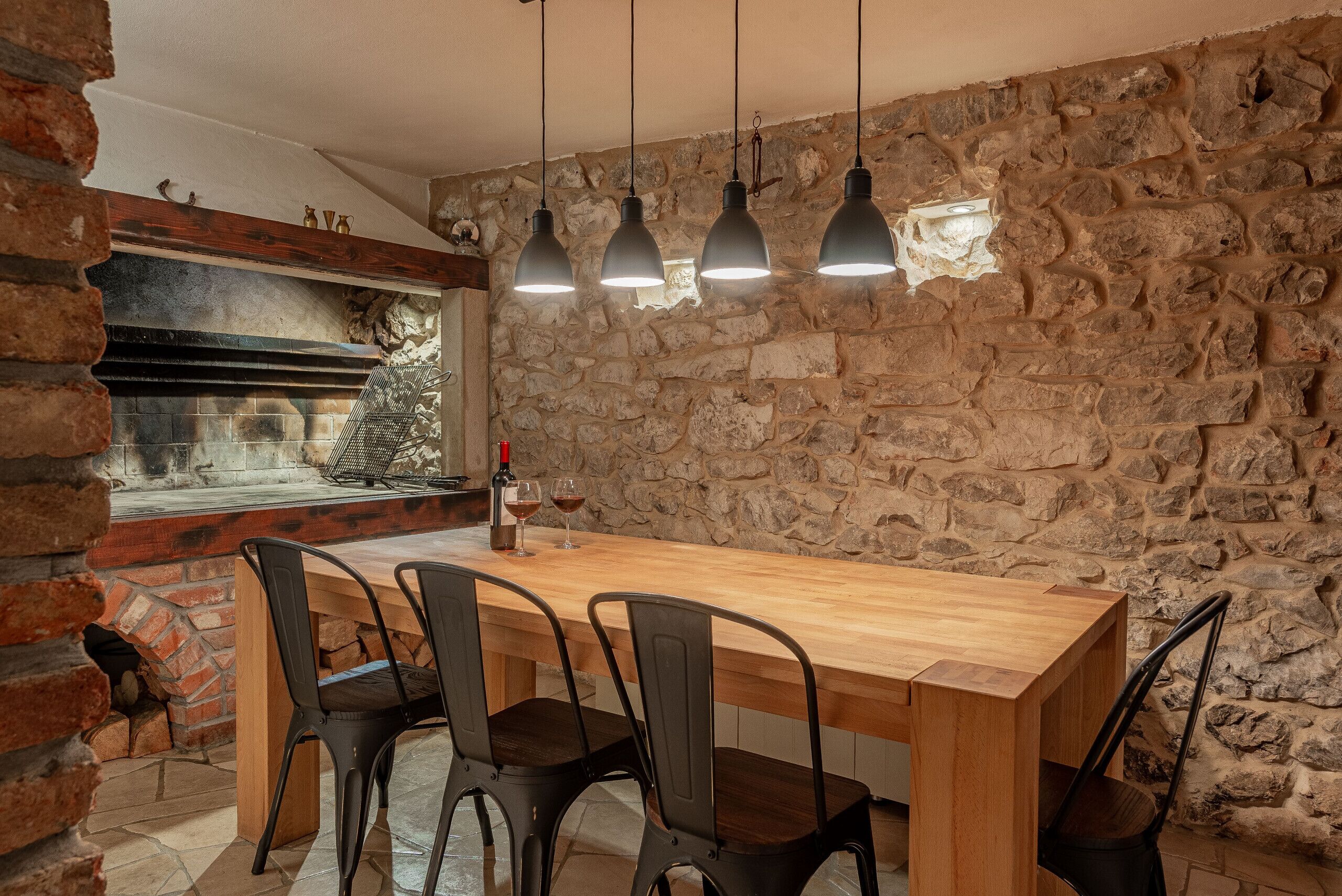 A rustic dining area with a stone wall, a wooden table, and black chairs.