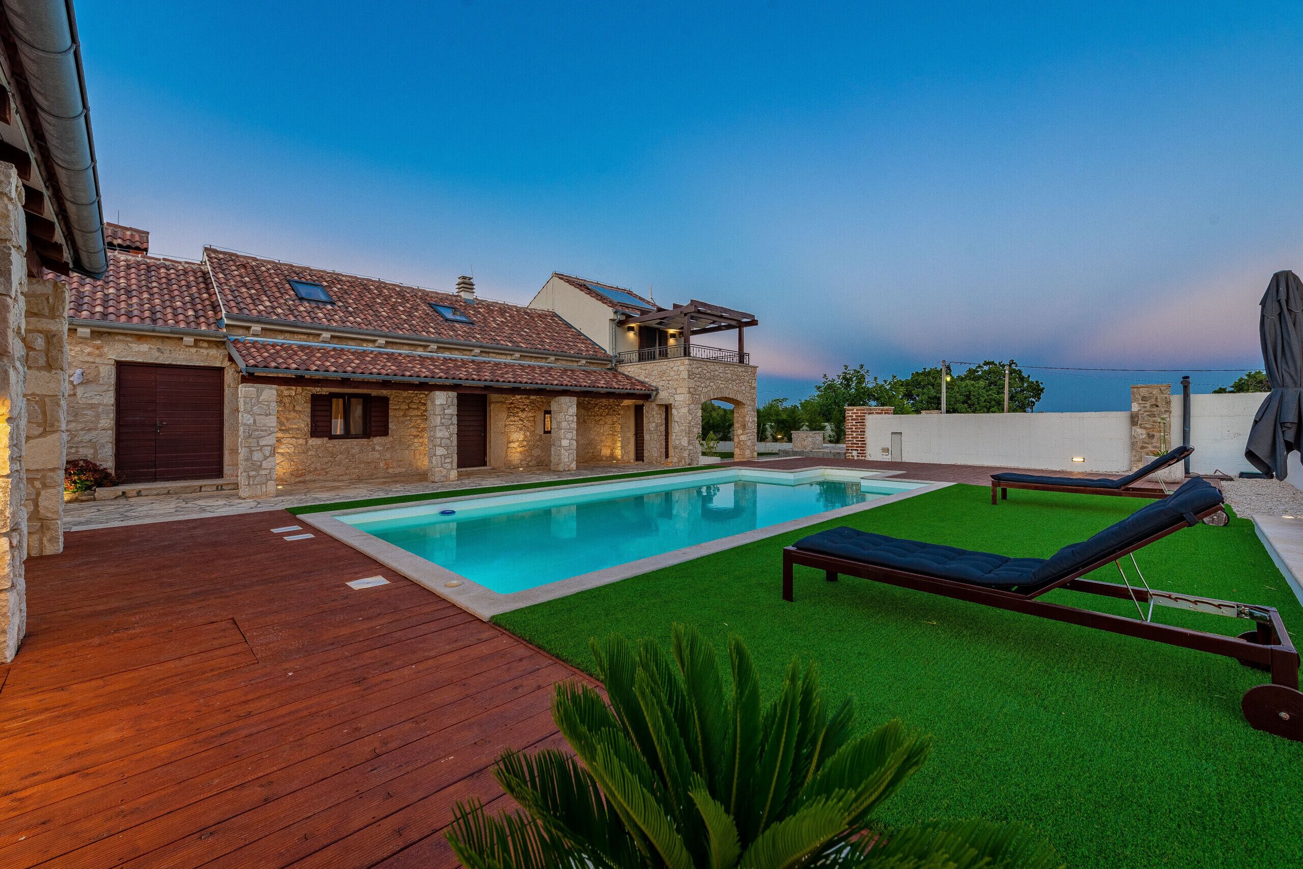 Une villa dotée d’une piscine, de murs en pierre et d’une terrasse en bois.