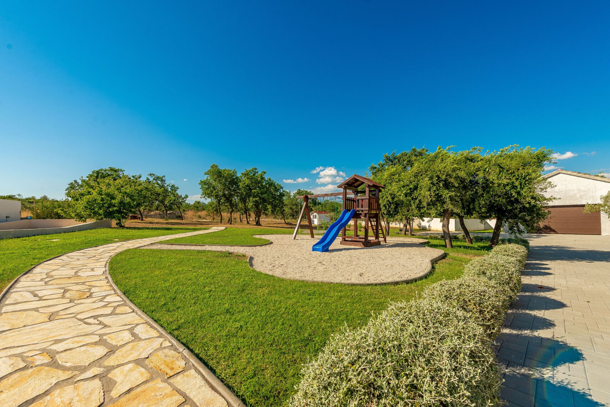 A playground with a slide, surrounded by a stone pathway and green grass.