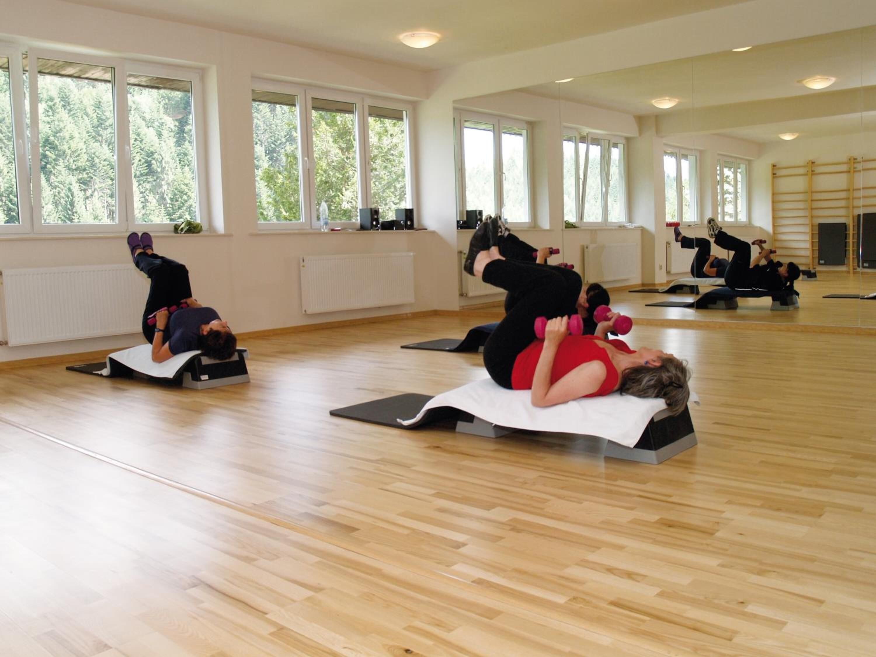 A spacious room with large windows, wooden flooring, and exercise mats.