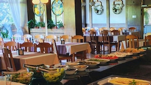 Un restaurante con varias mesas y sillas, un bufé con diversos platos y apliques decorativos en las paredes.