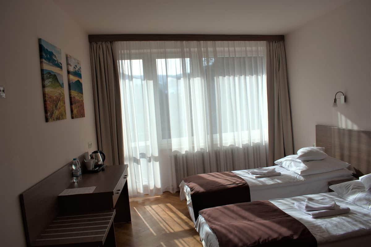 Ein Hotelzimmer mit zwei Betten, einem Schreibtisch und einem Fenster mit durchsichtigen Vorhängen.