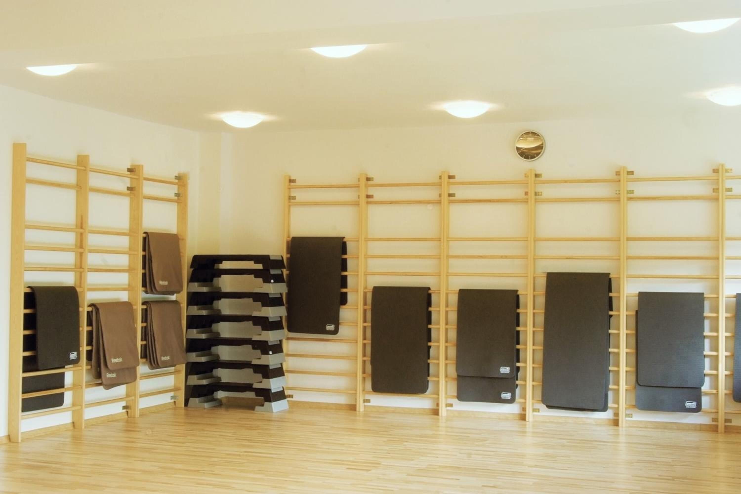 A room with wooden wall shelves holding folded mats, a wooden floor, and recessed ceiling lights.