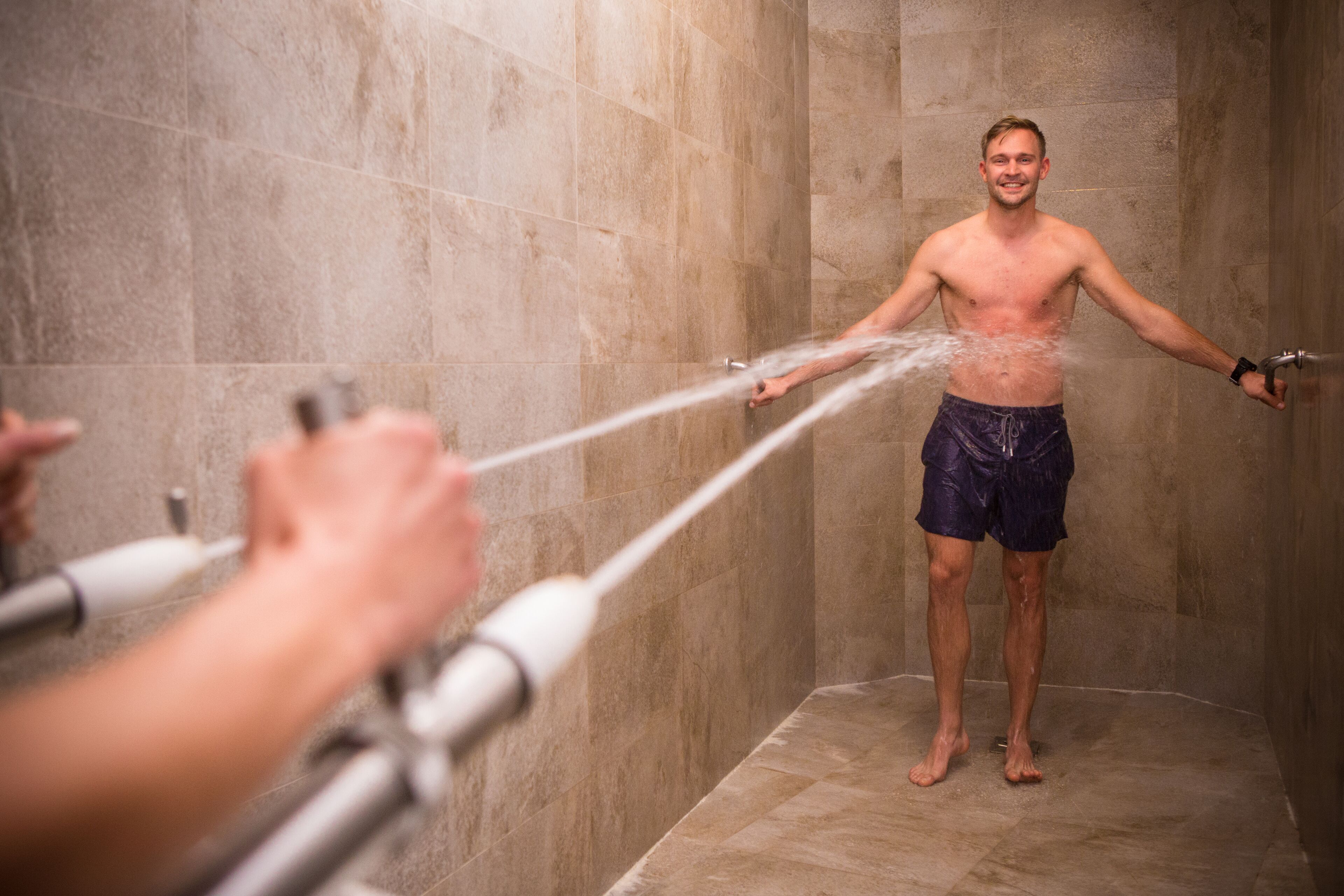 Un hombre en la ducha mientras el agua sale de un cabezal de ducha portátil.