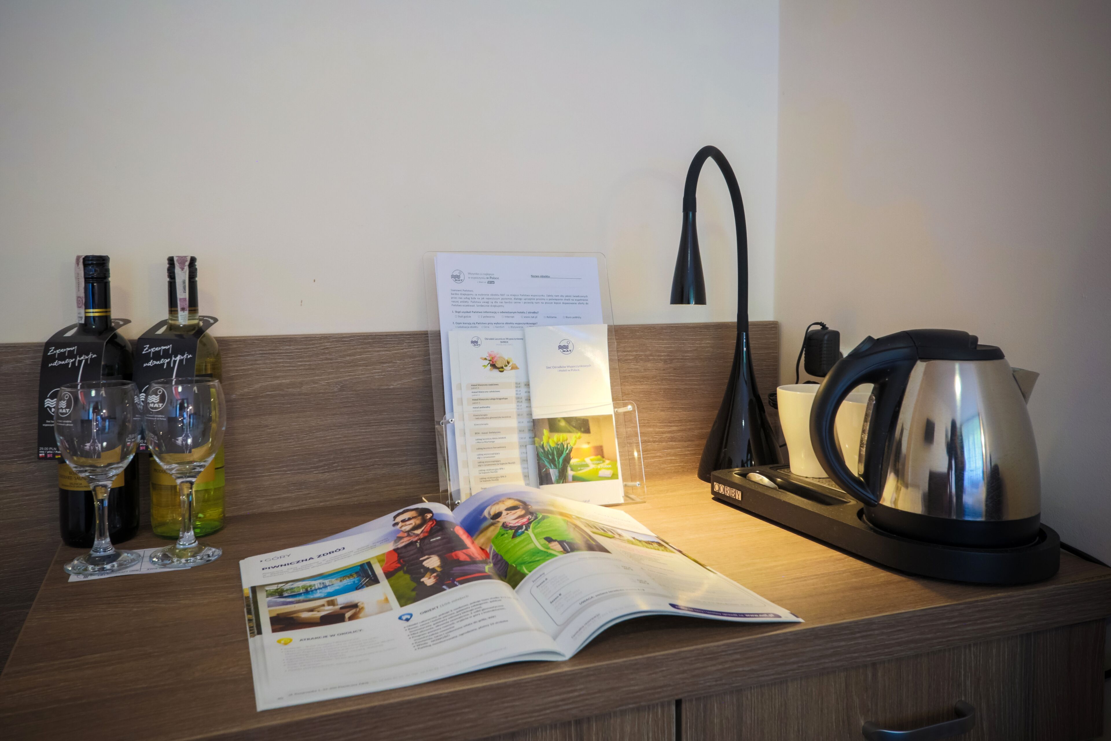 Una encimera de madera con dos botellas de vino, dos copas de vino, una revista, una tetera y una cafetera.