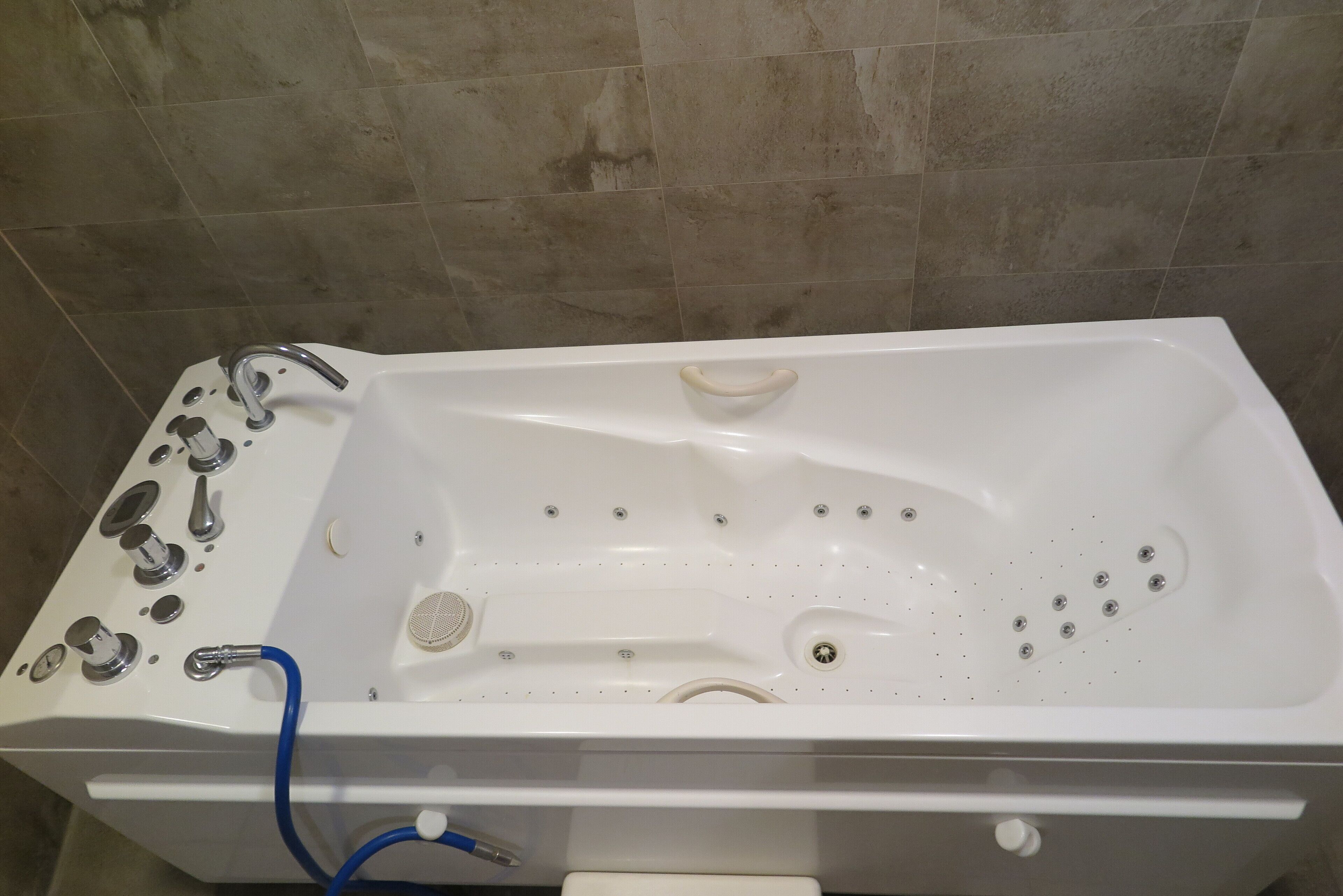A white bathtub with multiple faucets and a drain, set against a tiled wall.