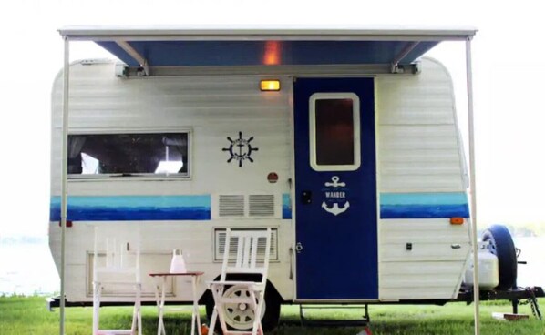 Una autocaravana con puerta azul identificada con la leyenda 'WANDER', una pequeña mesa y una silla en el exterior.
