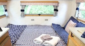 Un dormitorio compacto para autocaravana con cama, una mesita pequeña y una ventana con cortinas.