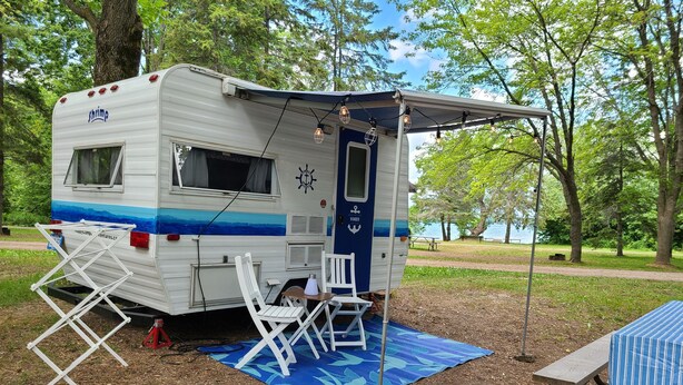 A mobile home with a covered porch, a table, and chairs set up on a blue mat. - Nautical Cozy camper trailer on Lake Simcoe (Orillia)