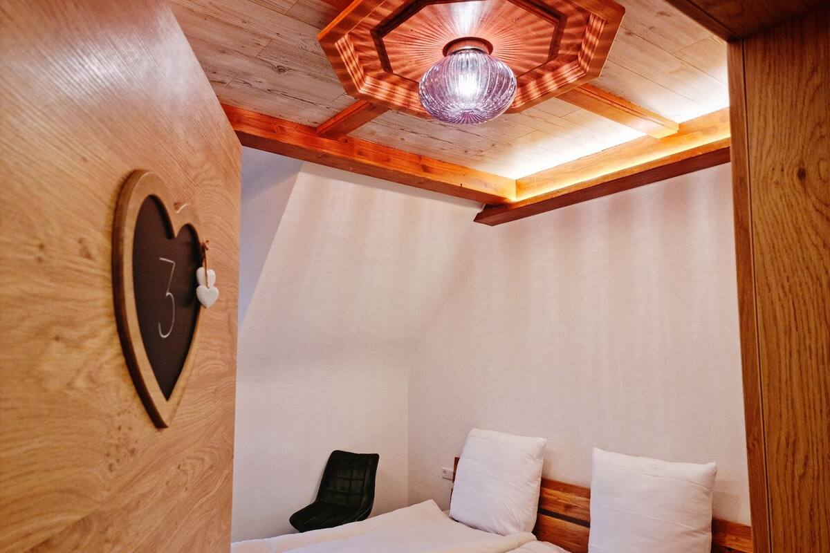 A cozy bedroom with a wooden ceiling, a bed with white bedding, and a unique hexagonal ceiling light fixture.