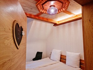 A cozy bedroom with a wooden ceiling, a bed with white bedding, and a unique hexagonal ceiling light fixture.