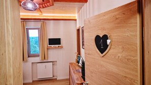 A wooden door with a heart-shaped decoration, a wooden dresser, a television on a shelf, and a window with curtains. - Wirtshaus Zum Löwen (Steinenbronn)
