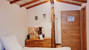 A bedroom with a wooden ceiling, a bed with white bedding, a dresser with a mirror, and a door with a sign. - Wirtshaus Zum Löwen (Steinenbronn)