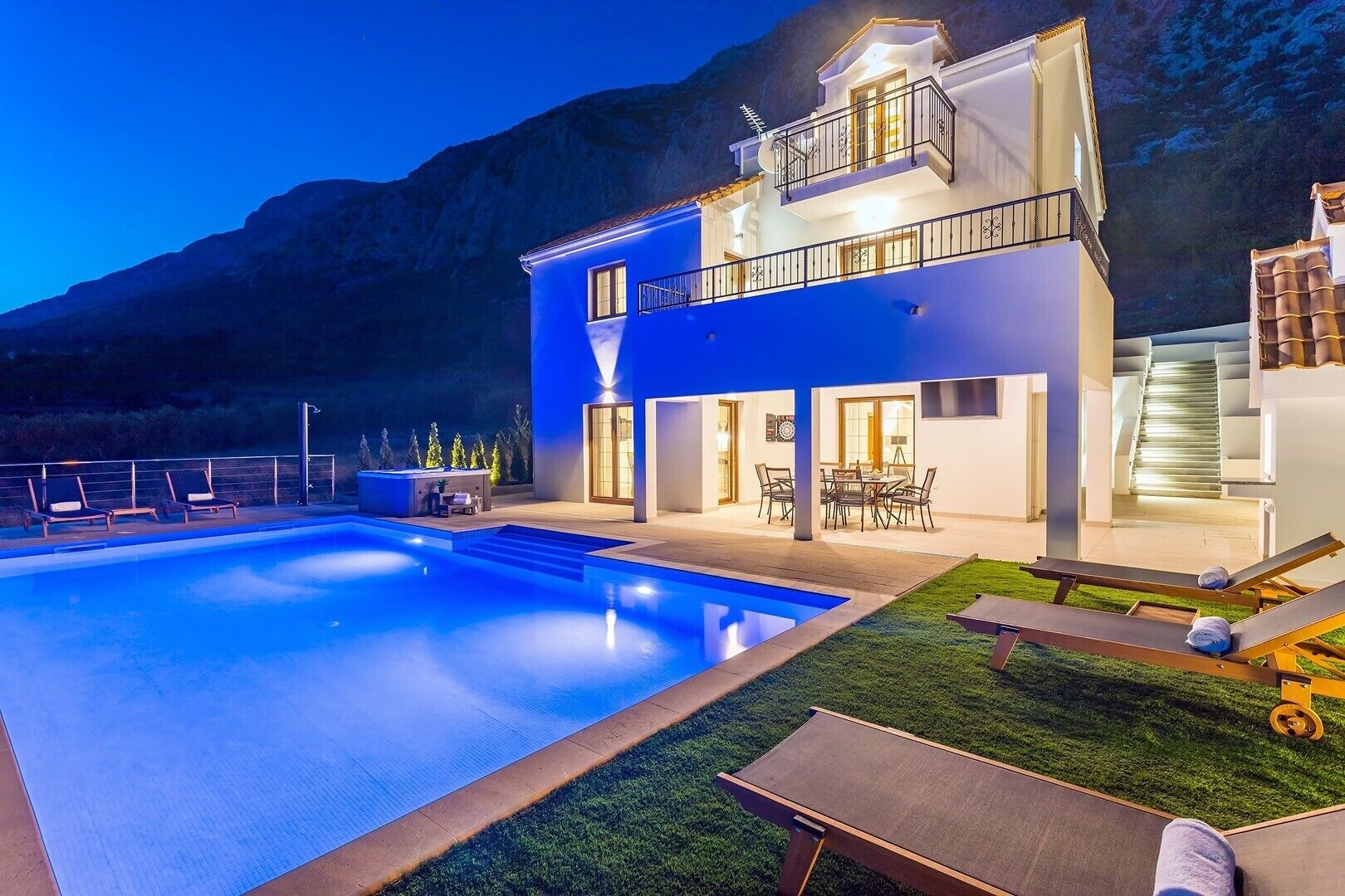 A modern two-story house with a swimming pool, outdoor seating, and a staircase leading to a balcony.