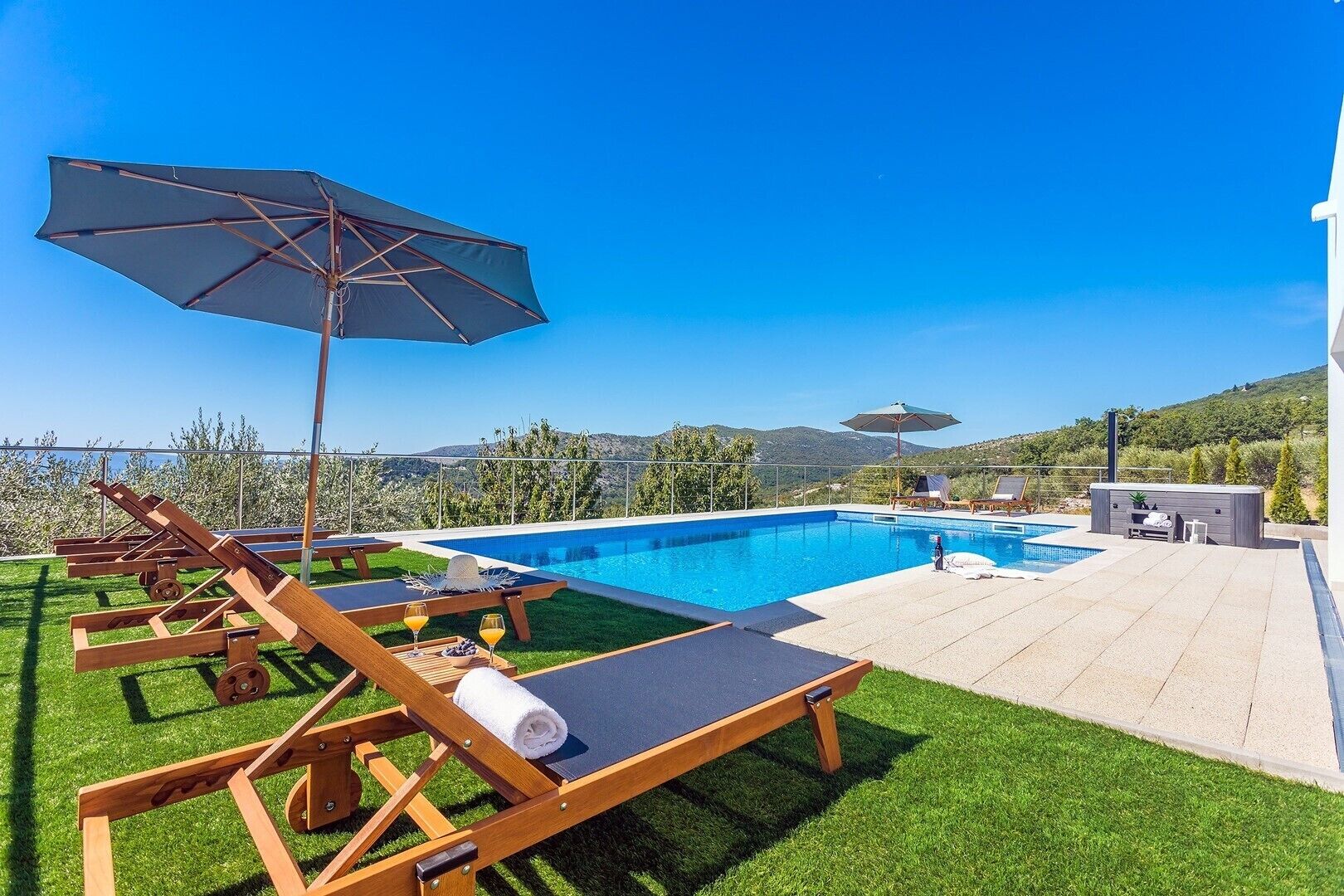A poolside area with lounge chairs, umbrellas, and a view of the mountains.