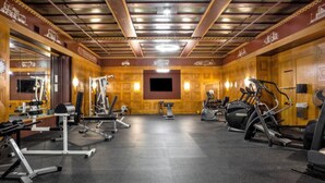 Un gimnasio con diversos equipos de ejercicio, un espejo grande y una pantalla de televisión en la pared.