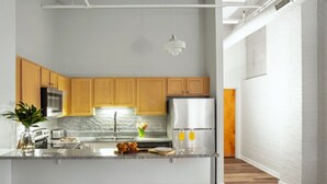 Una cocina moderna con armarios de madera, un refrigerador de acero inoxidable, una encimera de mármol y una zona de bar con taburetes.