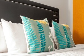 Een bed met wit beddengoed en twee kussens met een bladmotief.