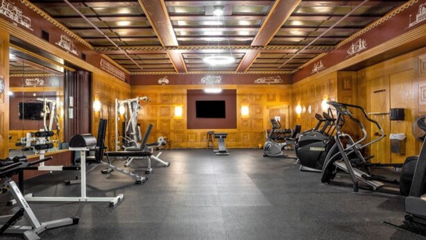 A gym with various exercise equipment, a large mirror, and wooden paneling on the walls. - Contemporary 2BR 2BA Apartment In Downtown Indianapolis by CozySuites (Indianapolis)