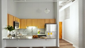 A modern kitchen with wooden cabinets, a central island with stools, stainless steel appliances, and a hanging pendant light. - TWO Bold 2BR 2BA Apartments by CozySuites (Indianapolis)