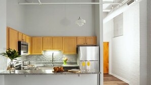 A modern kitchen with wooden cabinets, a marble countertop, a stainless steel refrigerator, and a bar area with stools. - TWO Urban 2BR 2BA Apartments by CozySuites (Indianapolis)