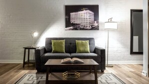 A modern living room with a grey sofa, two green cushions, a coffee table with an open book, a floor lamp, and a framed picture on the wall. - TWO Urban 2BR 2BA Apartments by CozySuites (Indianapolis)