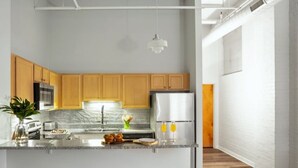 A modern kitchen with wooden cabinets, a marble countertop, and a central island with stools. - BOLD 2BR/2BA In The Block Apartment by CozySuites (Indianapolis)