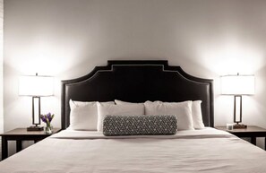 A neatly made bed with a black headboard, white pillows, and a patterned pillow. There are two bedside tables with lamps and a vase with flowers on one table. - BOLD 2BR/2BA In The Block Apartment by CozySuites (Indianapolis)