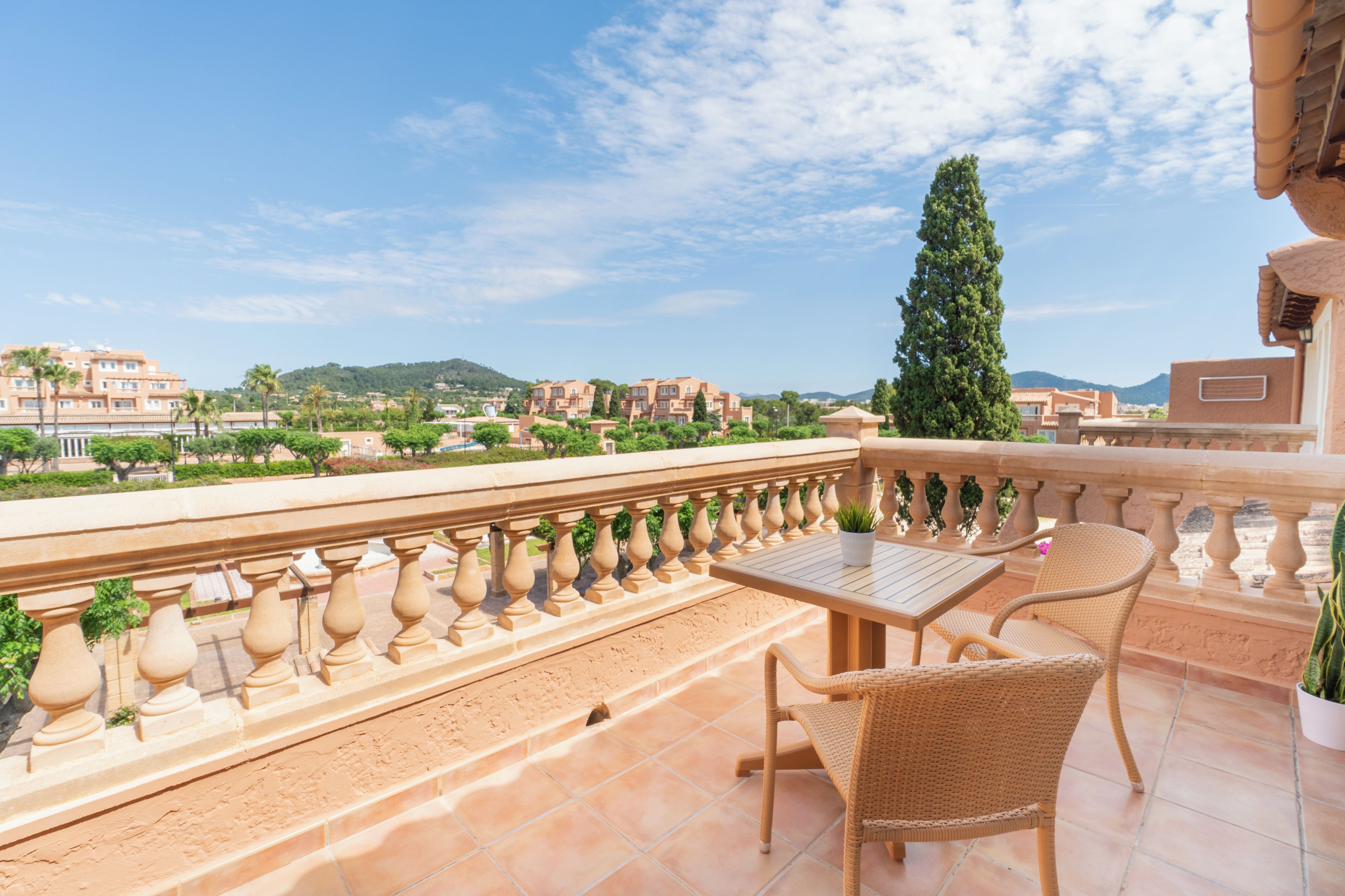 A balcony with a table and chairs, overlooking a residential area with houses and a mountain in the distance.