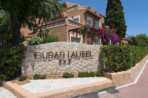 Un muro de piedra con la inscripción "CIUDAD LAUREL" y un edificio con balcones y techo de tejas.
